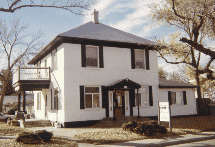 A white two-story house with dark trim, a side balcony and an Almost Home yard sign