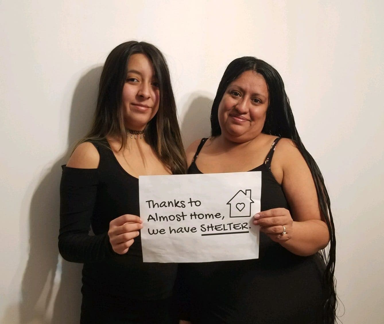 A mother and her teenage daughter hold a sign: Thanks to Almost Home, we have SHELTER.