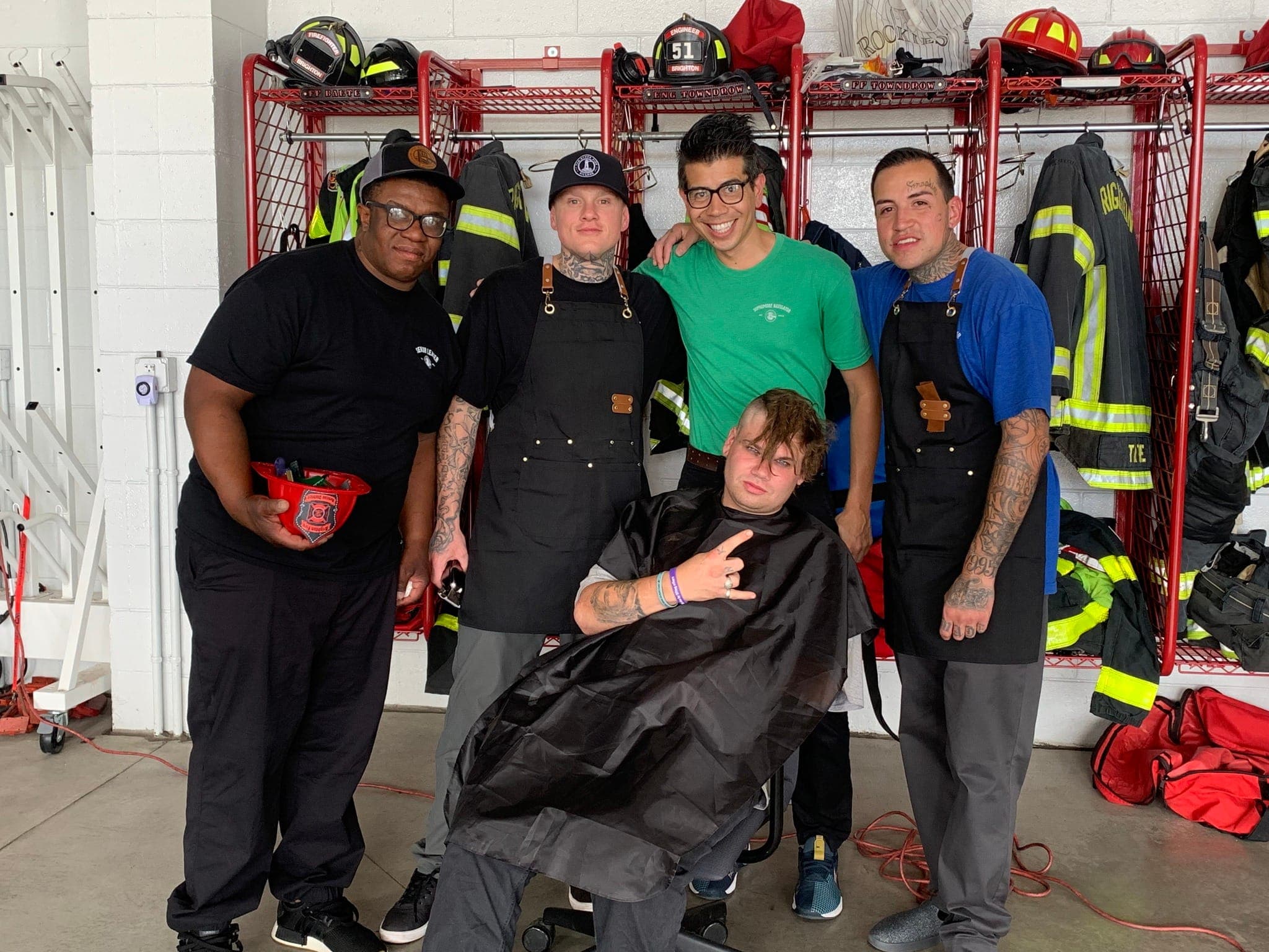 Volunteer barbers in aprons with a client after a free haircut in a Brighton fire station