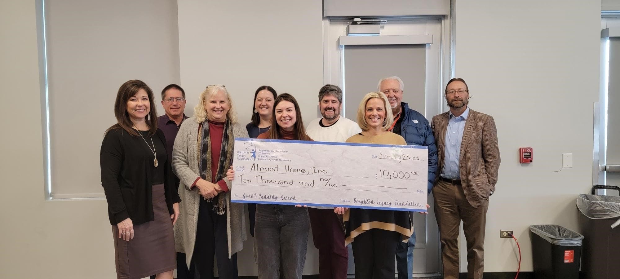 Nine people holding a $10,000 Brighton Legacy Foundation grant check made out to Almost Home
