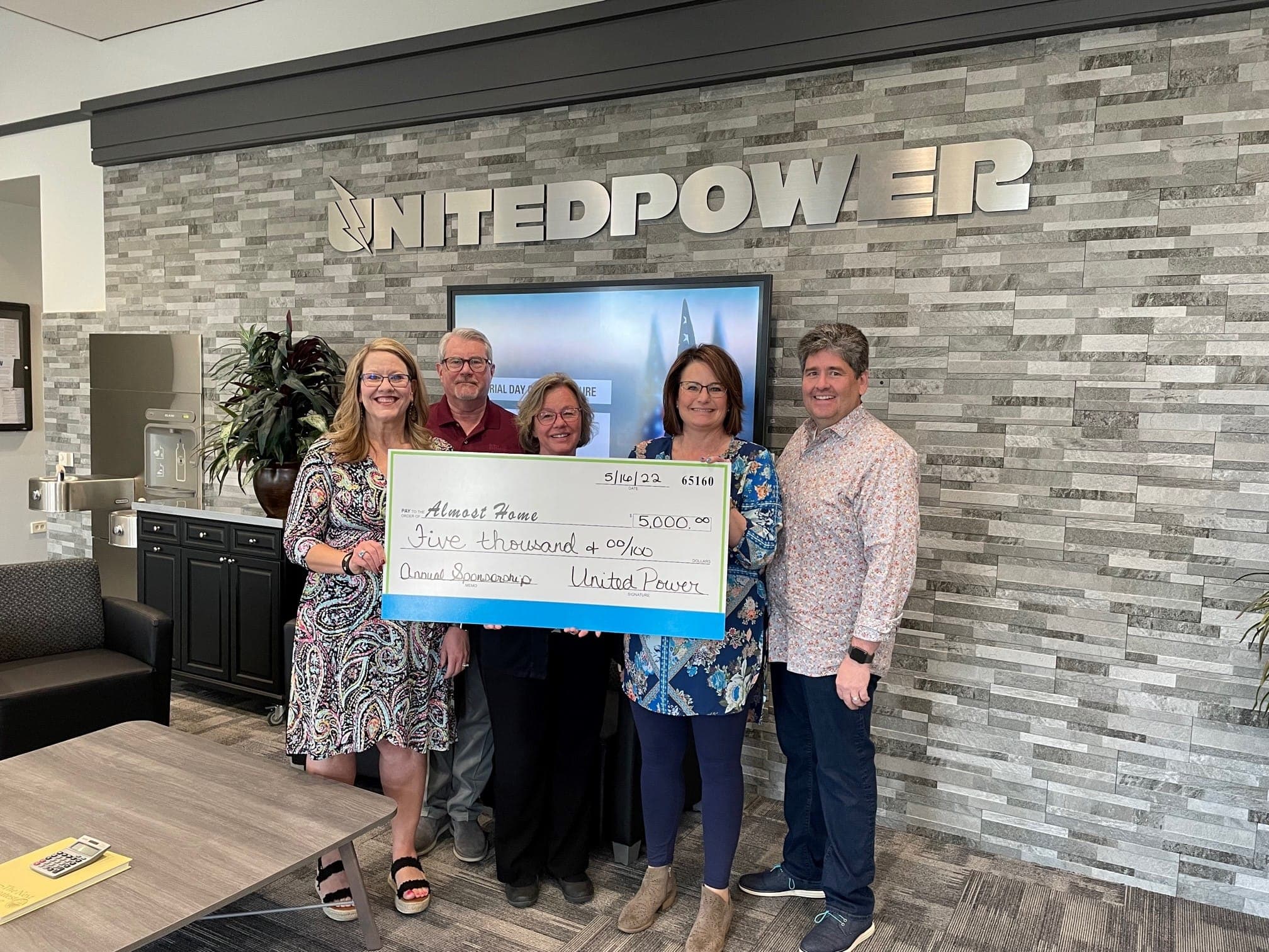 Five people in the United Power lobby holding a $5,000 annual sponsorship check made out to Almost Home