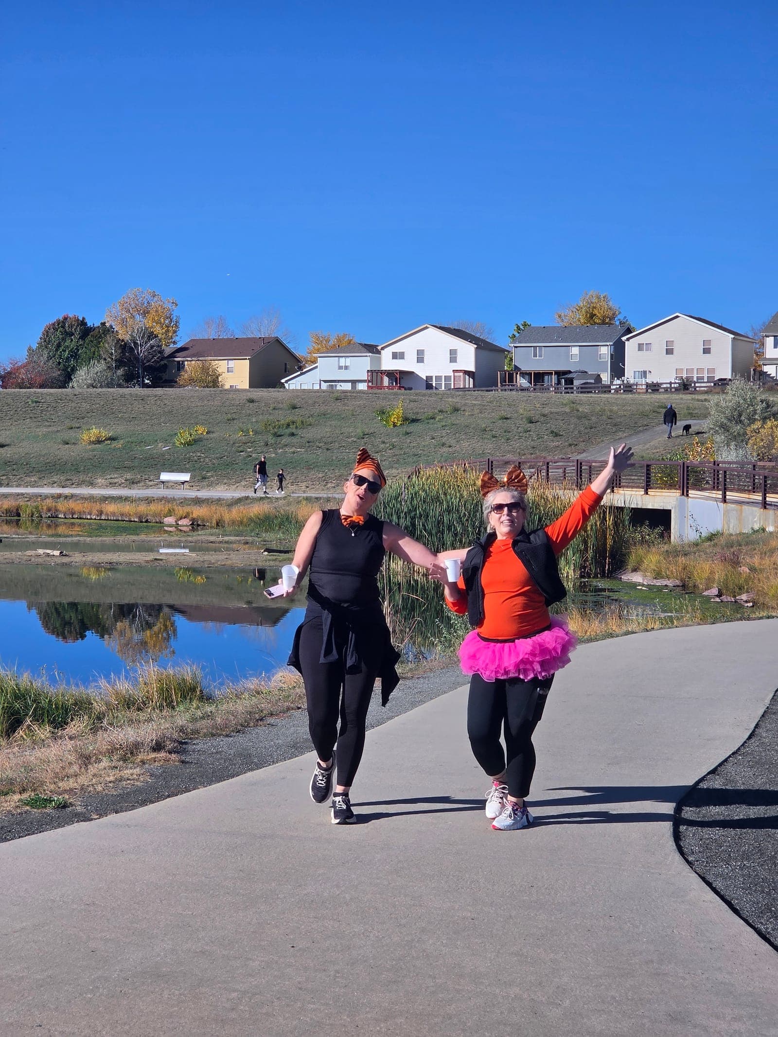 Two Spooky Sprint 5K walkers in costume, tiger ears and a pink tutu, on a lakeside path