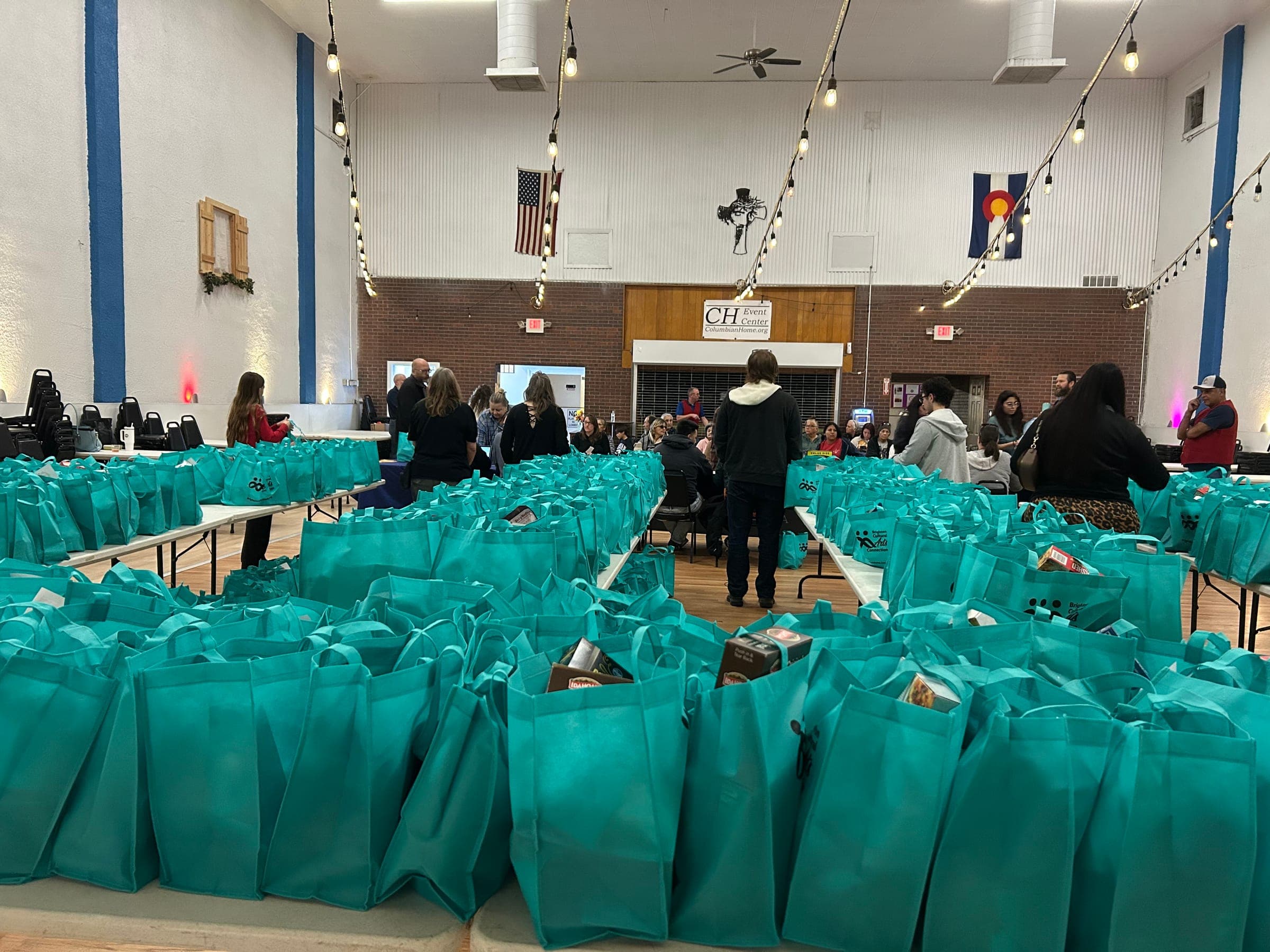 Hundreds of teal Thanksgiving meal bags lined up on tables at the Columbian Home event hall